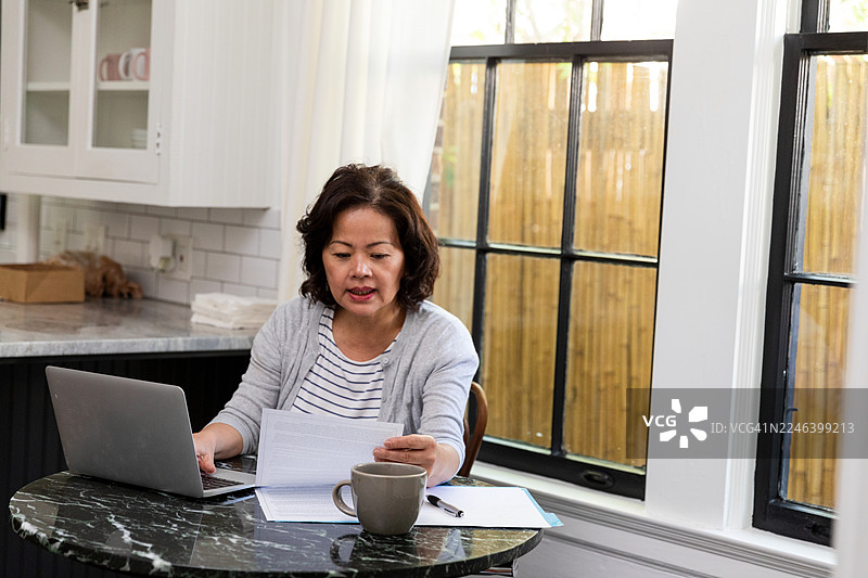 亚洲女性在家中办公室的笔记本电脑上工作，旁边有文件和咖啡。咖啡。咖啡。图片素材