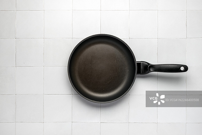 白色瓷砖地板上黑色不粘特氟龙涂层平底锅的俯视图图片素材