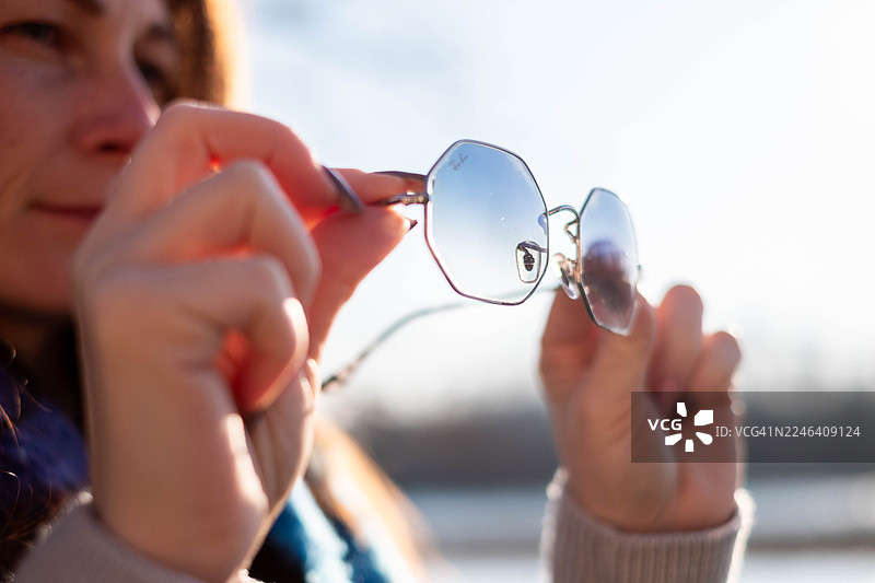 女子在户外拿着时尚的蓝色雷朋太阳镜图片素材