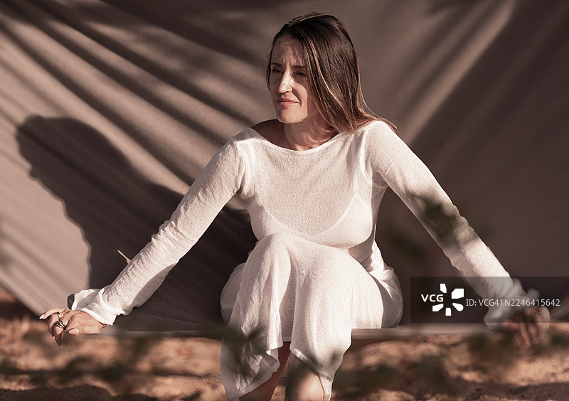 身穿白裙的年轻女子坐在户外，阳光斑驳图片素材