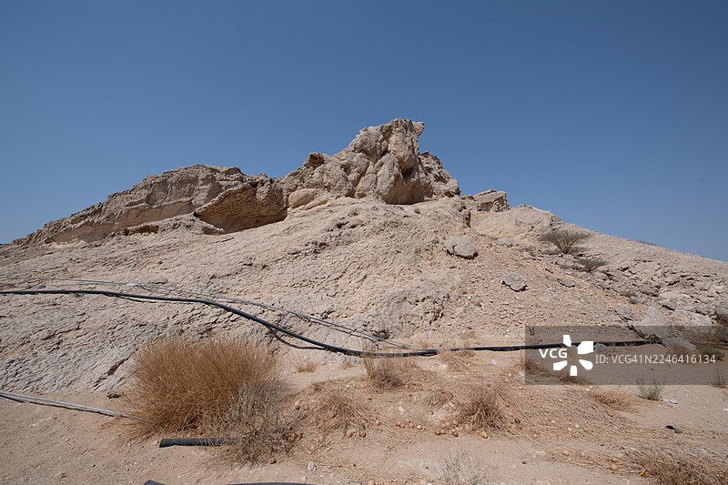 从低角度看，荒漠景观中崎岖的岩石构造在晴朗的蓝天下，阿联酋艾因，哈菲特山图片素材