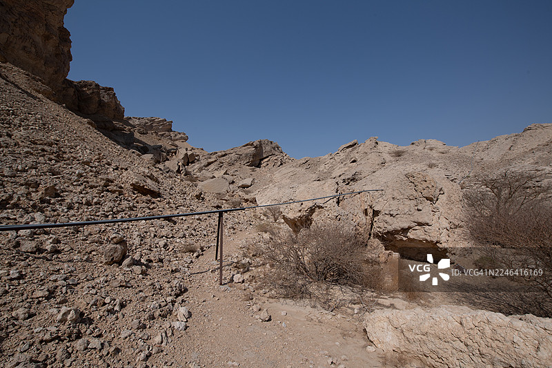 低角度拍摄，晴朗蓝天下岩石山脉，前景为金属栏杆，阿联酋艾因，杰贝勒哈菲特图片素材