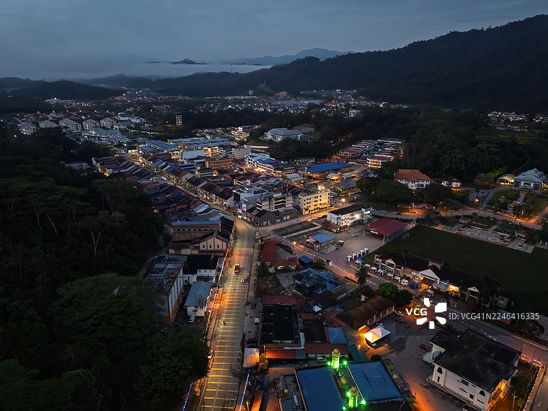 俯瞰夜间灯火辉煌的城市，城市坐落在黑暗的山脉和茂密的森林之间图片素材