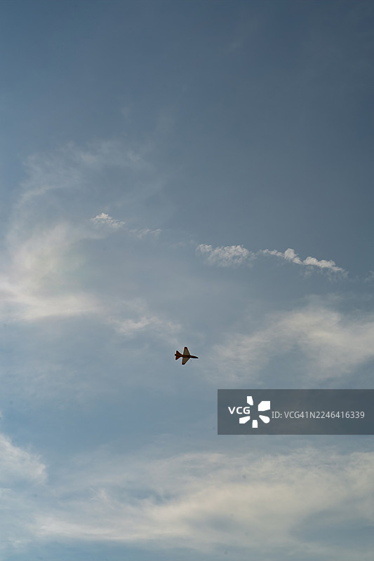 低角度仰视，一架喷气式飞机在高耸的蓝天中，伴着缕缕白云飞行。图片素材