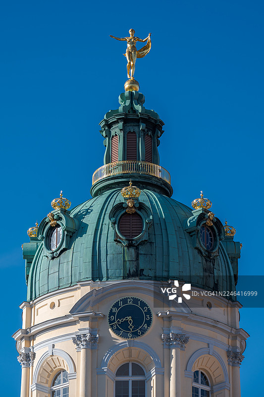 从低角度仰视一座圆顶建筑顶部的金色雕像，背景是湛蓝的天空，展现了建筑细节和历史的优雅，德国，柏林，夏洛滕堡宫图片素材