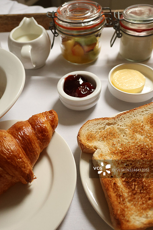 白色桌面上丰盛美味的早餐，俯视角度拍摄，包括羊角面包、吐司、水果、果酱、黄油和牛奶图片素材