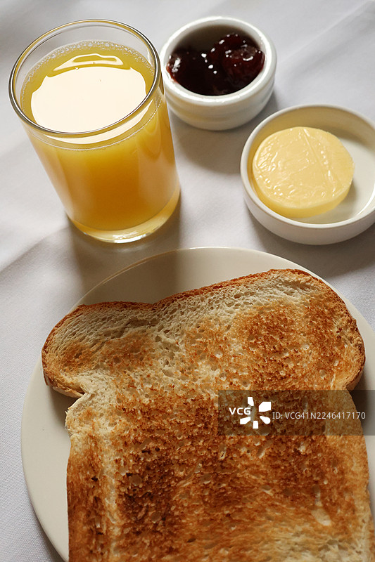 俯视视角，一张铺着白色桌布的简约而诱人的早餐，包含吐司、橙汁、果酱和黄油图片素材