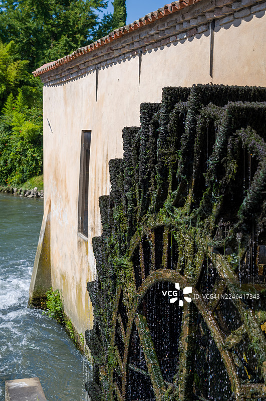 阳光明媚的一天，意大利波尔托格鲁阿罗，一座古老的石头建筑旁，历史悠久的水磨坊，巨大的木制水车上覆盖着苔藓和藻类，正在流淌的河流中转动。图片素材