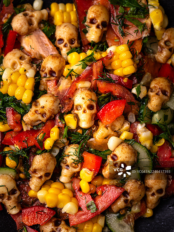 万圣节主题沙拉的俯视特写，碗中有骷髅造型食物、玉米、甜椒和香草图片素材
