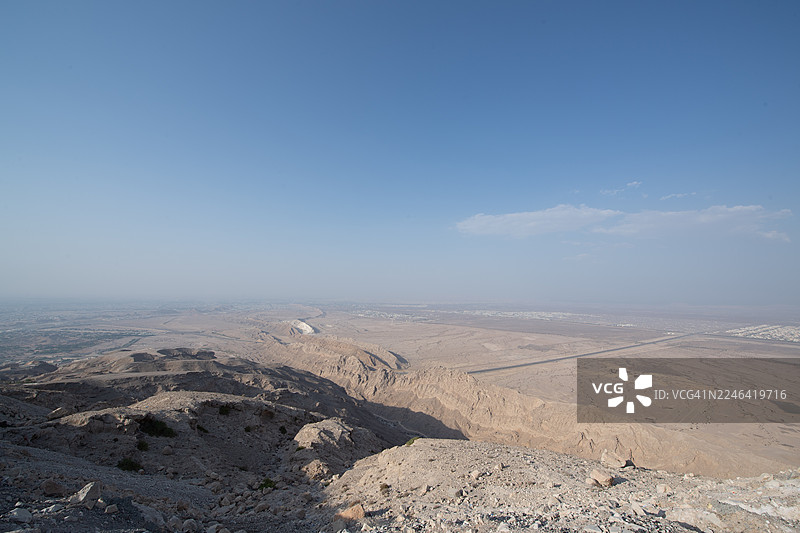 广阔的沙漠风光，天空晴朗，远方有山脉和道路，地点：阿联酋艾恩，杰贝勒哈菲特图片素材
