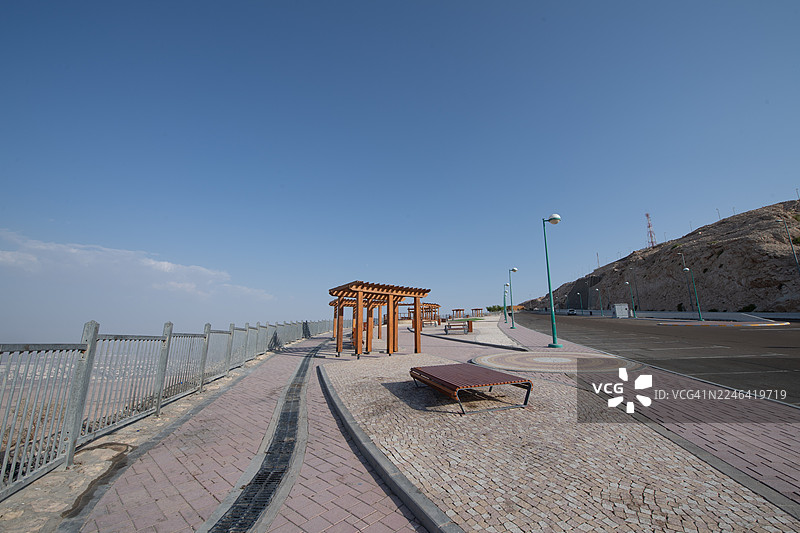 晴朗蓝天下，山海相连处的空旷道路与铺砌步道，设有木质凉棚和长椅，位于阿联酋艾因的杰贝勒哈菲特。图片素材