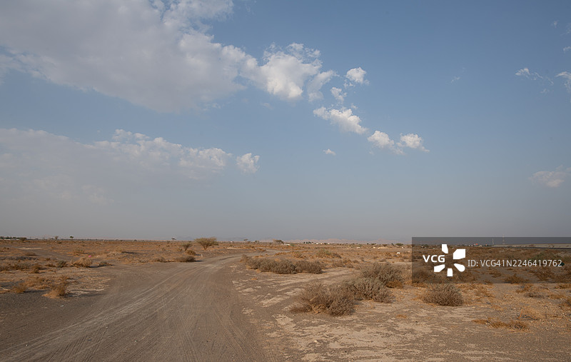延绵起伏的土路穿过干旱的田野，在广阔的蓝天下，点缀着几朵白云，阿联酋艾因，杰贝勒哈菲特图片素材