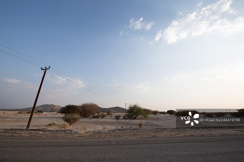 晴朗天空下的沙漠景观，有电线杆和电线，位于阿联酋艾因的杰贝勒哈菲特图片素材
