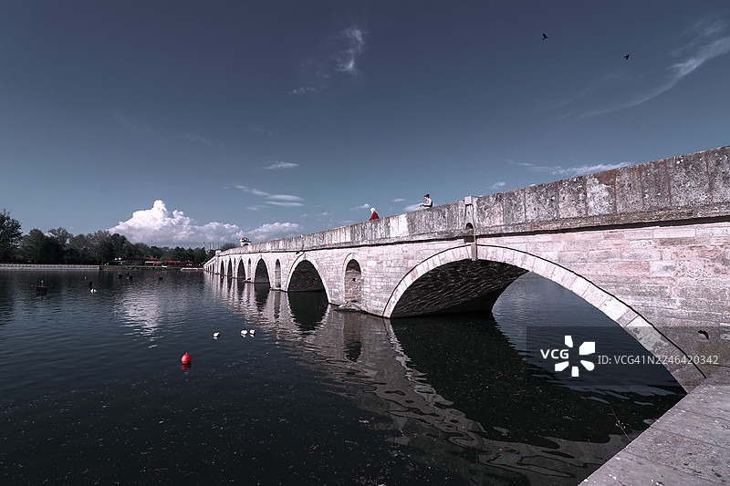 土耳其埃迪尔内，蓝天下宁静河流上的历史石头拱桥图片素材