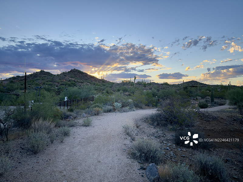 日落时分沙漠风光，有山脉和蜿蜒小路，阳光穿透云层，位于美国斯科茨代尔北阿尔玛学校公园大道。图片素材
