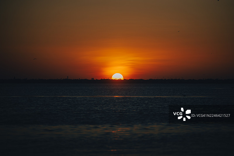 橙色天空倒映在平静的海面上，呈现出壮丽的日落景象图片素材