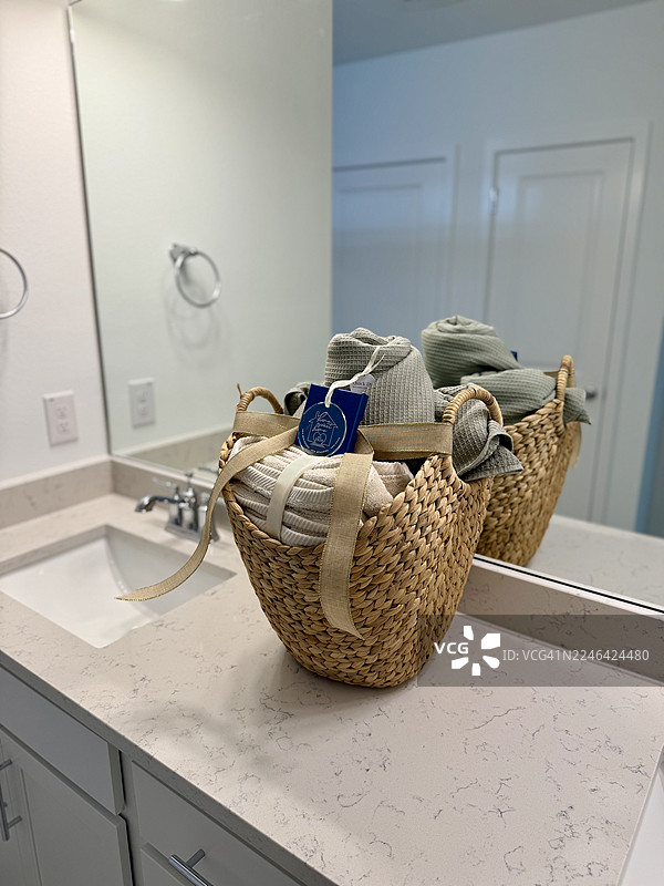 浴室梳妆台上放着一个装满毛巾的编织篮的特写，镜子里映照出房间的景象图片素材