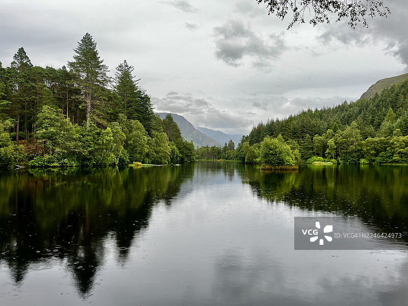 宁静的湖面倒映着云天下的葱郁森林和群山图片素材