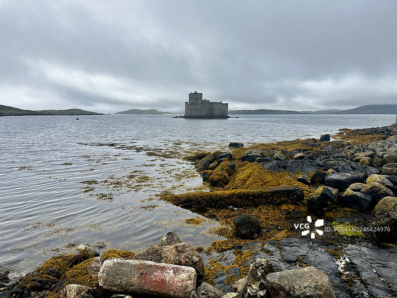 历史悠久的基西穆尔城堡雄伟地坐落在一个小岛上，周围是宁静的海湾，海湾的岸边覆盖着岩石和海藻，天空多云。图片素材