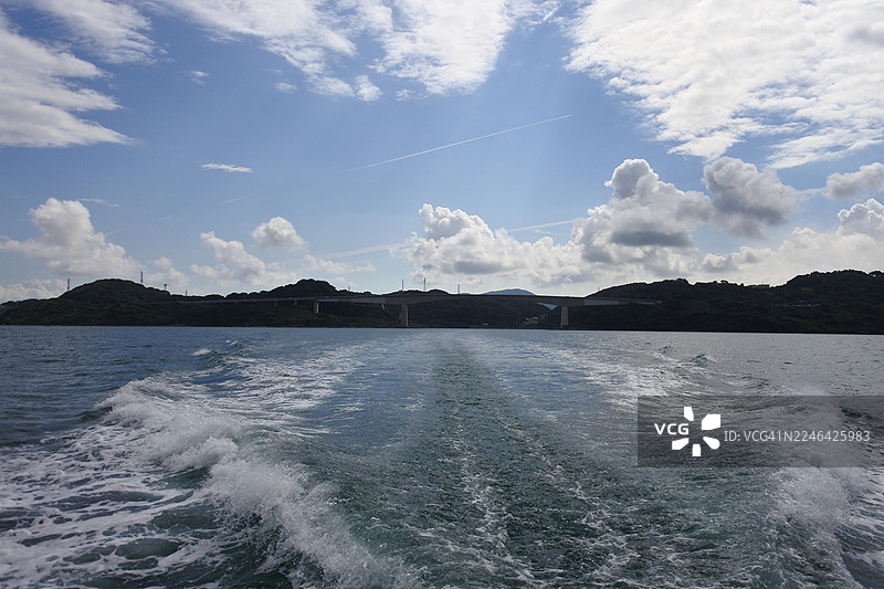船在多云天空下的海上航行，远方有陆地和桥梁，日本，JP图片素材