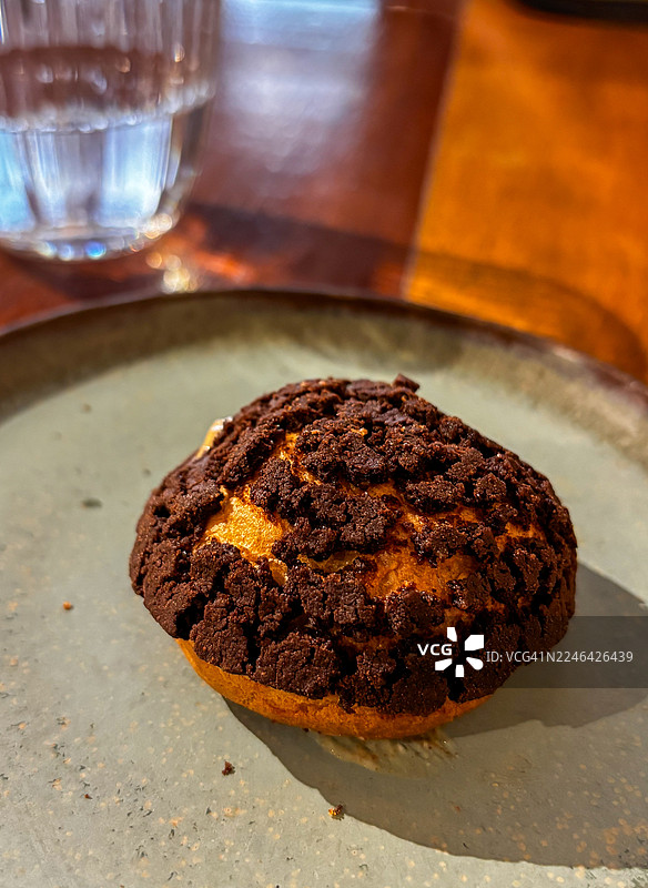 一个装在灰色盘子里的美味巧克力泡芙的特写，旁边放着一杯水，背景色彩温暖图片素材