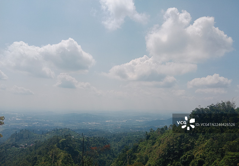 印度尼西亚三宝垄，晴朗多云的天空下，郁郁葱葱的绿色山峦与远处的平原构成了一幅广阔的宁静自然风光画卷图片素材