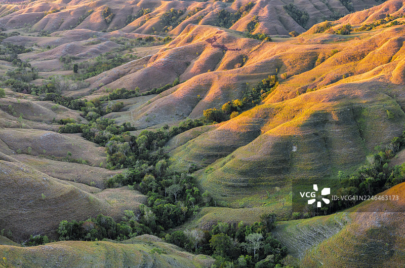 戏剧性的鸟瞰全景捕捉了印度尼西亚松巴岛独特起伏的山丘和广阔的开阔地貌，在动态的天空下展现。在日落时分，见证这个偏远而迷人的目的地原始、狂野的美景。图片素材