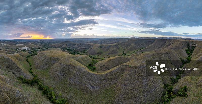 从空中俯瞰，印度尼西亚松巴岛独特起伏的山丘和广阔的开阔地貌在动态天空下呈现出戏剧性的全景。在日出时分，见证这个偏远迷人目的地原始、未经雕琢的美丽。图片素材