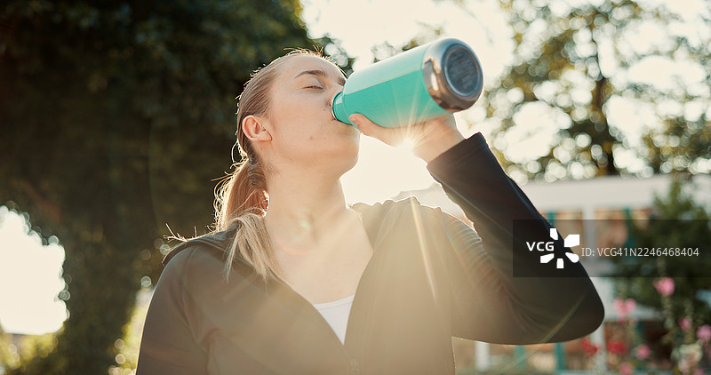 在公园里喝水健身的女性，休息和补充水分以促进健康，进行训练或排毒。一名女性，跑步者，在户外带着水瓶，进行锻炼和短暂休息，补充电解质，这是她在丹麦的日常训练的一部分。图片素材