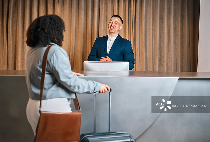 在酒店前台，一位商务男士在客人带着行李入住时微笑着图片素材