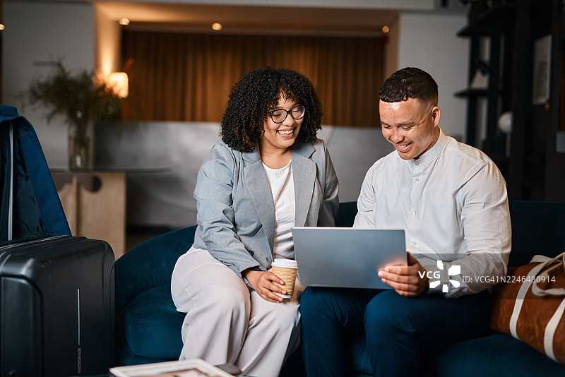 两位专业人士在机场酒店大堂共享笔记本电脑和咖啡，愉快地协作图片素材