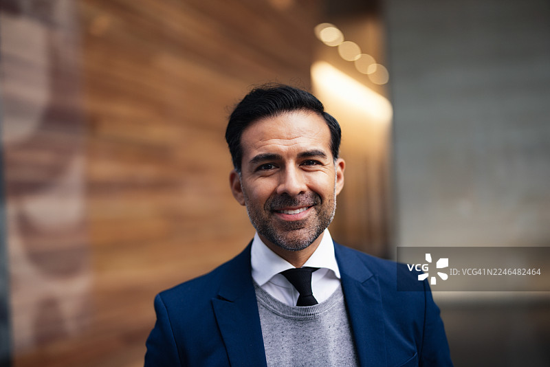 身着海军蓝西装的自信商人，在城市户外背景下微笑，拍摄专业肖像照。图片素材