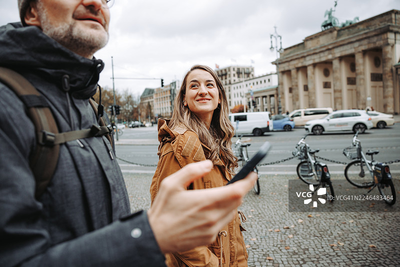 勃兰登堡门前，一位成熟的男士正使用智能手机，旁边还有一位年轻的女士。图片素材