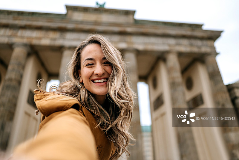 穿着休闲、面带微笑的女子在柏林勃兰登堡门前自拍图片素材