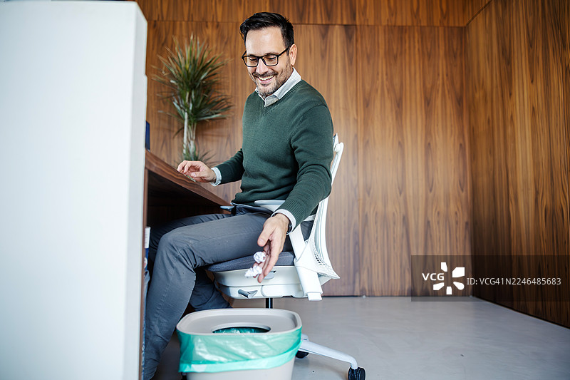 商人正在办公室的垃圾桶里笑着回收揉皱的纸张图片素材