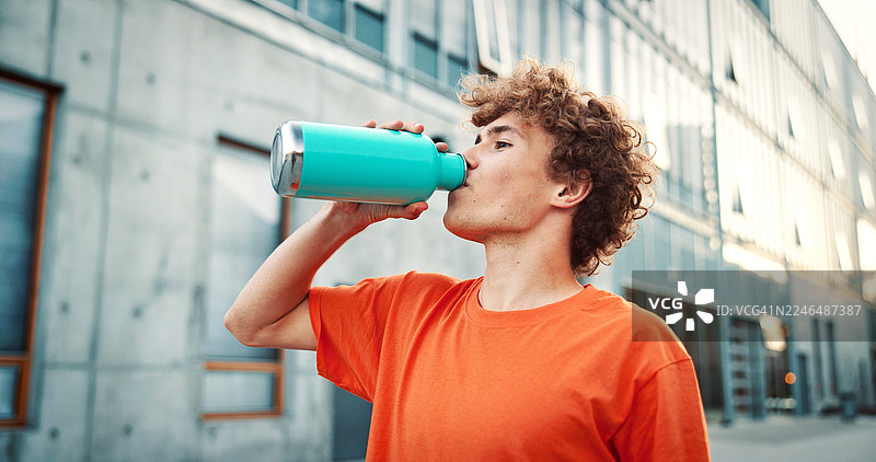 城市中，一名积极的男性正在饮用瓶装水，用于运动补水、锻炼或休息。健身、口渴的人在户外饮用饮料，以补充电解质、促进健康或达成健康体魄的目标。图片素材