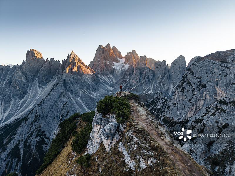 一名男子站在悬崖上，背景是意大利多洛米蒂山区的米苏里纳卡迪尼峰。图片素材