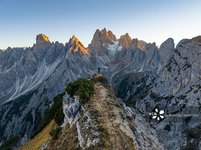 一名男子站在悬崖上，背景是意大利多洛米蒂山区的卡迪尼迪米苏里纳峰。图片素材