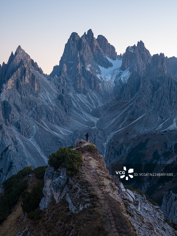 一名男子站在悬崖上，背景是意大利多洛米蒂山脉的米苏里纳卡迪尼峰。图片素材