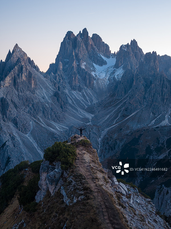 一名男子站在悬崖上，背景是意大利多洛米蒂的米苏里纳卡迪尼山峰图片素材