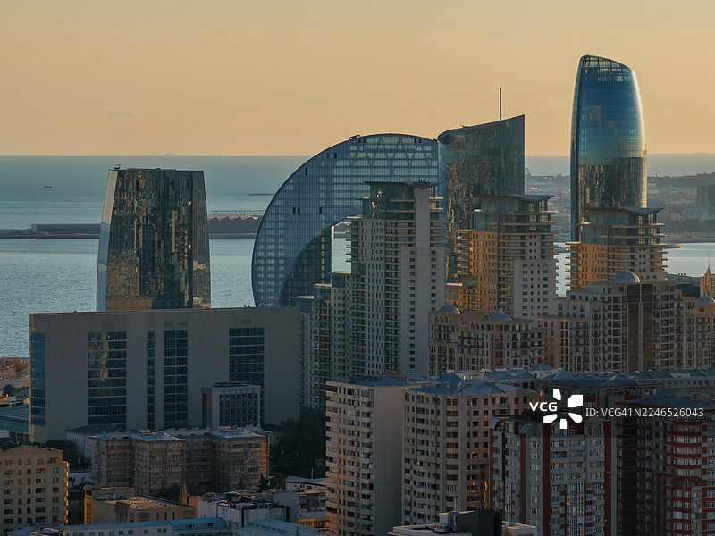 现代化的巴库天际线，拥有独特的玻璃塔楼和拱形摩天大楼，背景是里海附近柔和的金色傍晚天空。图片素材