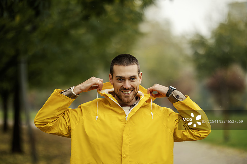 年轻男子穿着黄色雨衣在公园里微笑图片素材