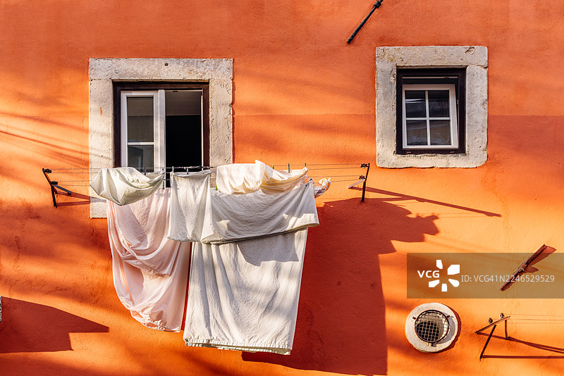葡萄牙里斯本阿尔法玛区，洗衣后干净的床单在橙色墙壁前的晾衣绳上晾晒图片素材