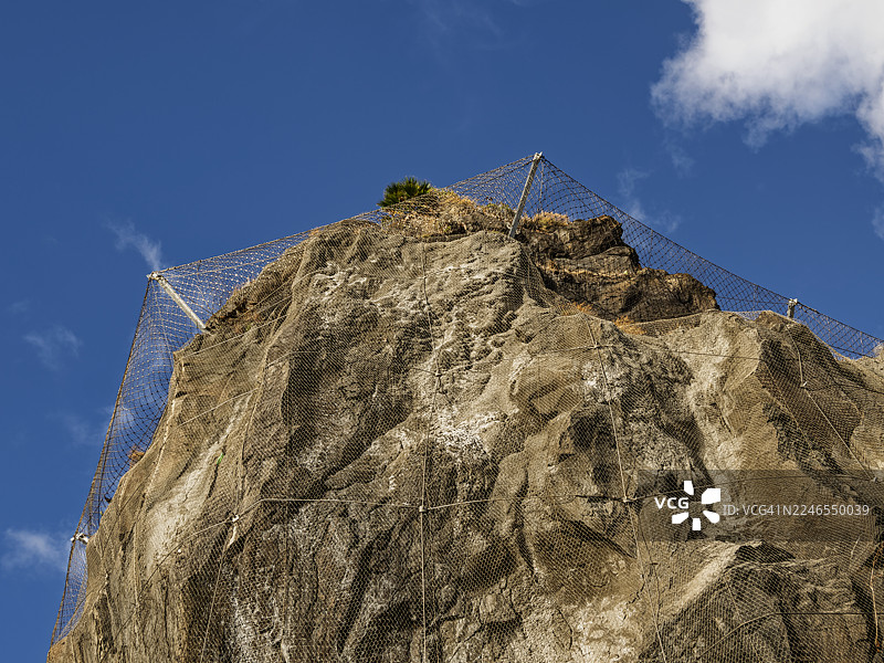 低角度拍摄，金属安全网支撑着一块巨大的火山岩。图片素材