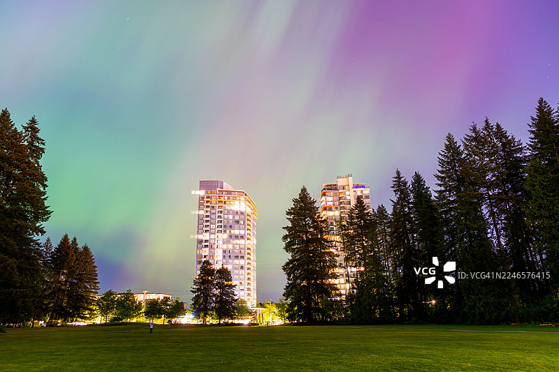 绚烂的北极光照亮城市建筑和葱郁公园上方的夜空图片素材