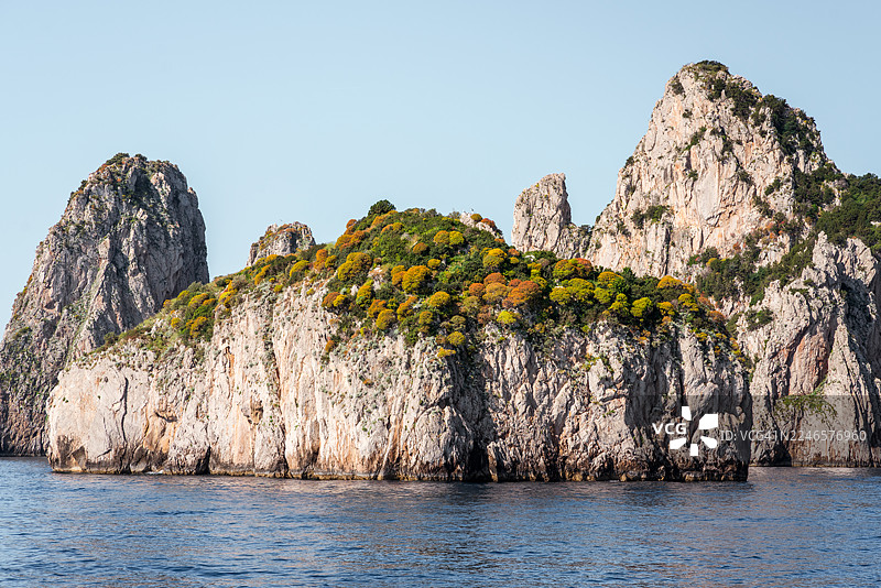 崎岖的海岸岩石从清澈的蓝色海洋中升起，在明媚的天空下，展现出粗犷的自然风光和宁静的海水图片素材