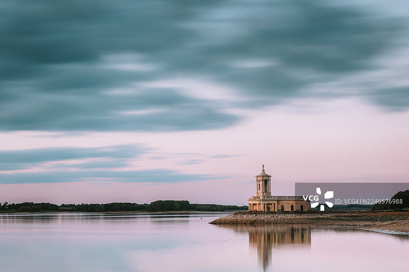 日落时分，英国奥克瑟姆，鲁特兰水域诺曼顿教堂在戏剧性的多云天空下的宁静景色图片素材