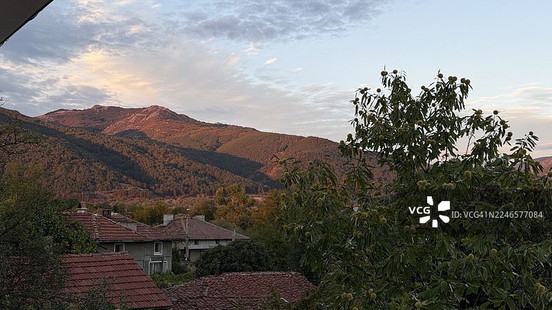 保加利亚克林，科姆索莫尔斯卡，日落时分，多云天空下的山脉和村庄屋顶的风景图片素材