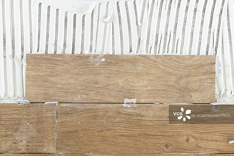 特写：在涂有粘合剂的墙面上安装木纹陶瓷瓷砖图片素材