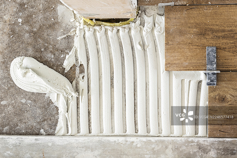 特写镜头：新鲜的瓷砖粘合剂铺在混凝土地板上，旁边是木板，准备铺设瓷砖，展示家庭装修或建筑工程。图片素材